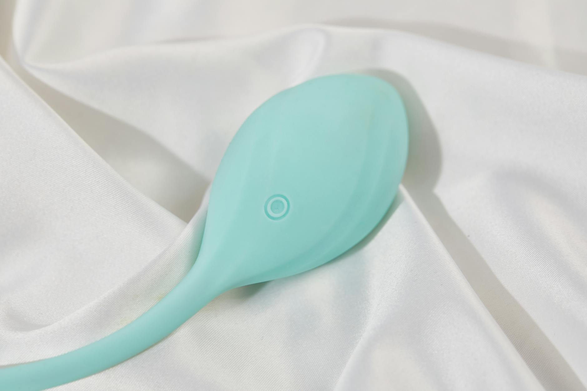 A teal lemon suction toy resting on soft white silk fabric, representing smooth texture and pleasure