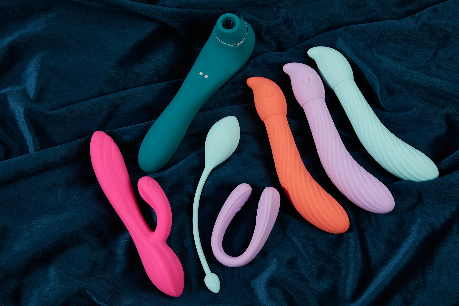 Collection of colorful silicone vibrators and clitoral toys displayed on dark fabric