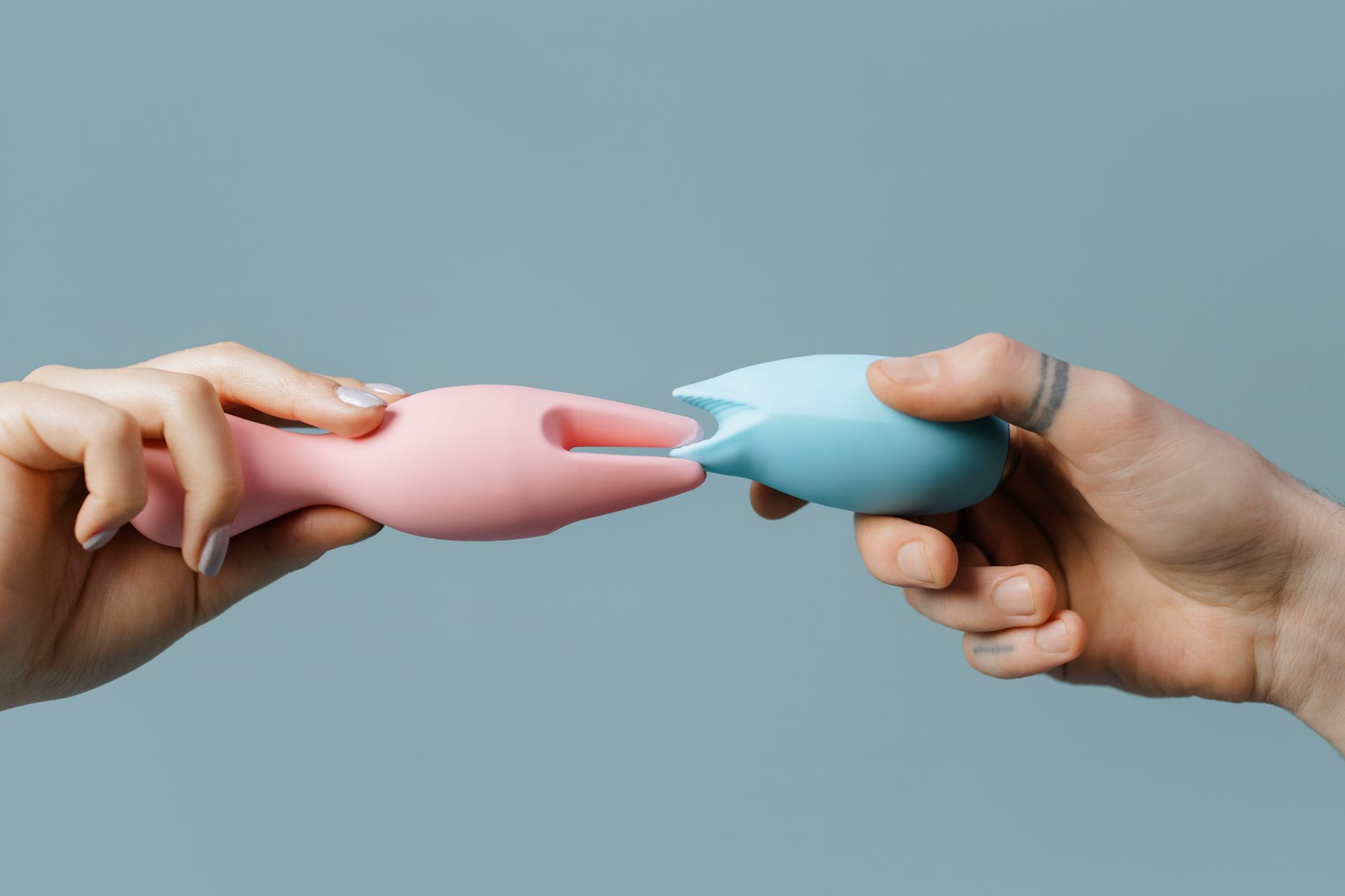 Two hands reaching for colorful silicone vibrators on a neutral surface