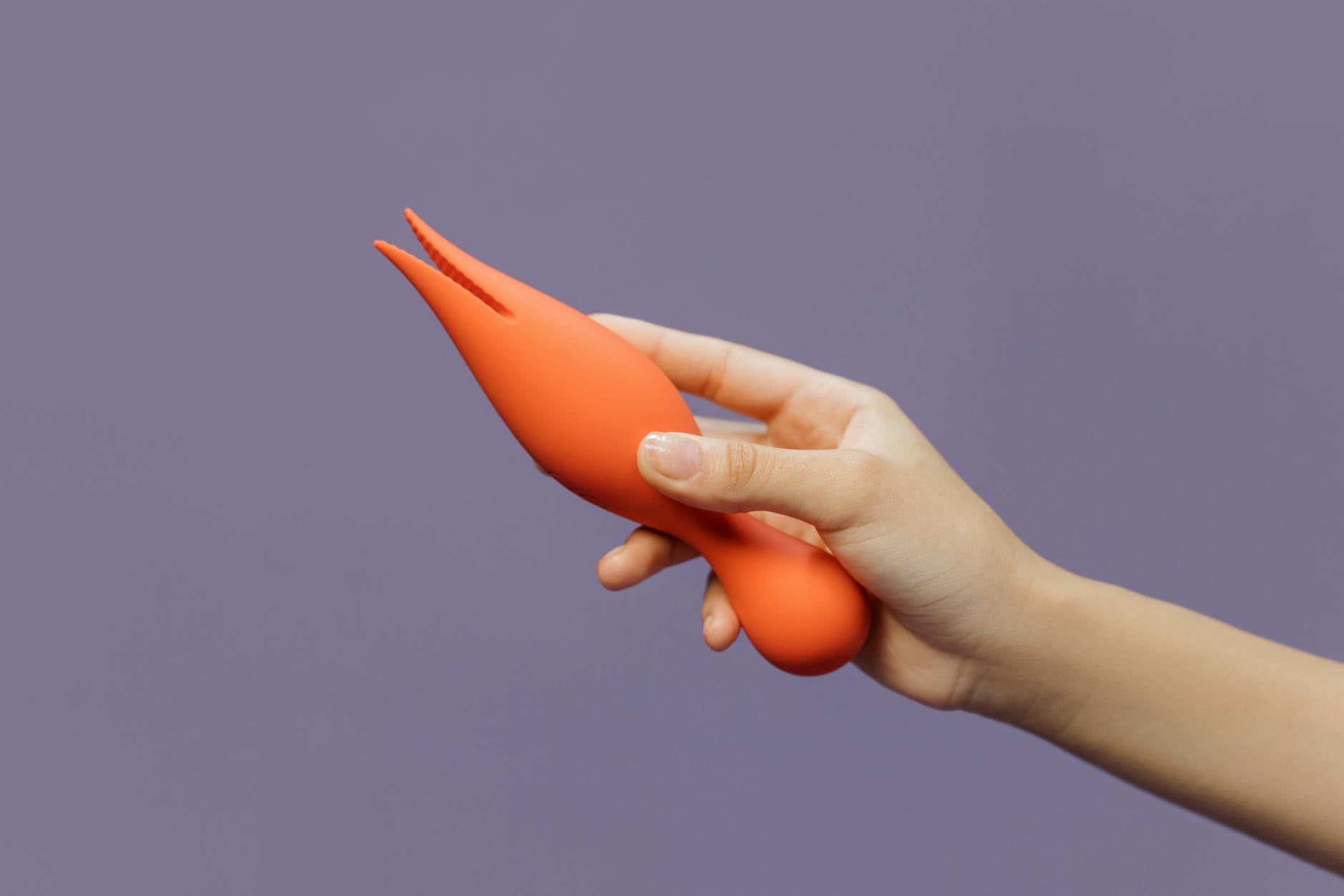 A hand holding an orange lemon vibrator against a minimalistic purple backdrop, showcasing modern sensuality.