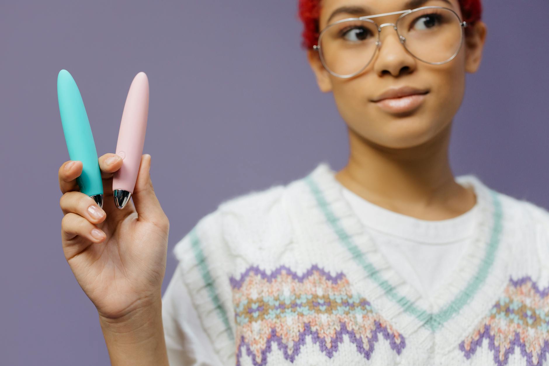 A woman holding colorful vibrators against a purple background, exploring pleasure tools