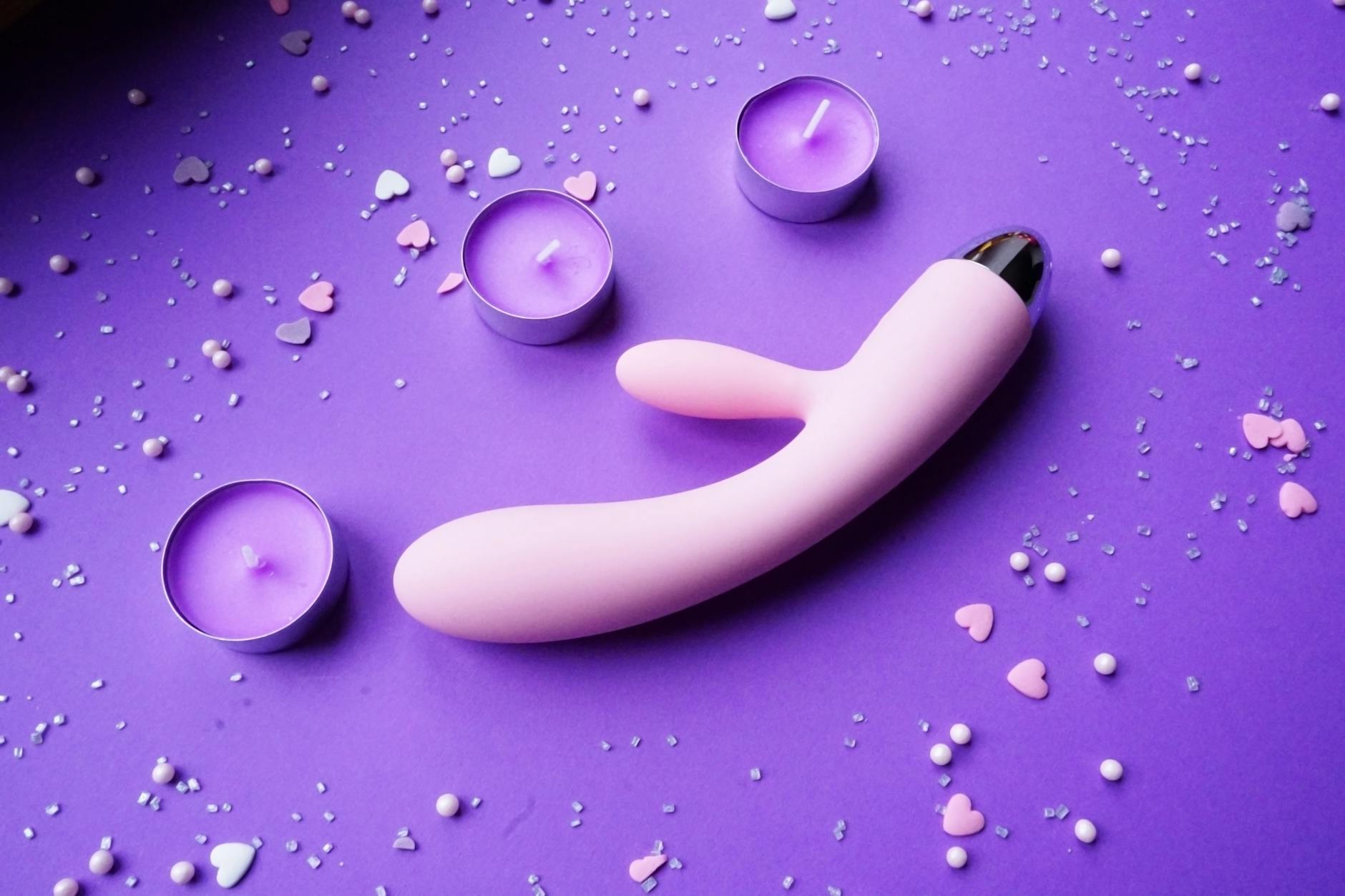 Pink lemon vibrator on purple background with romantic candles and heart confetti